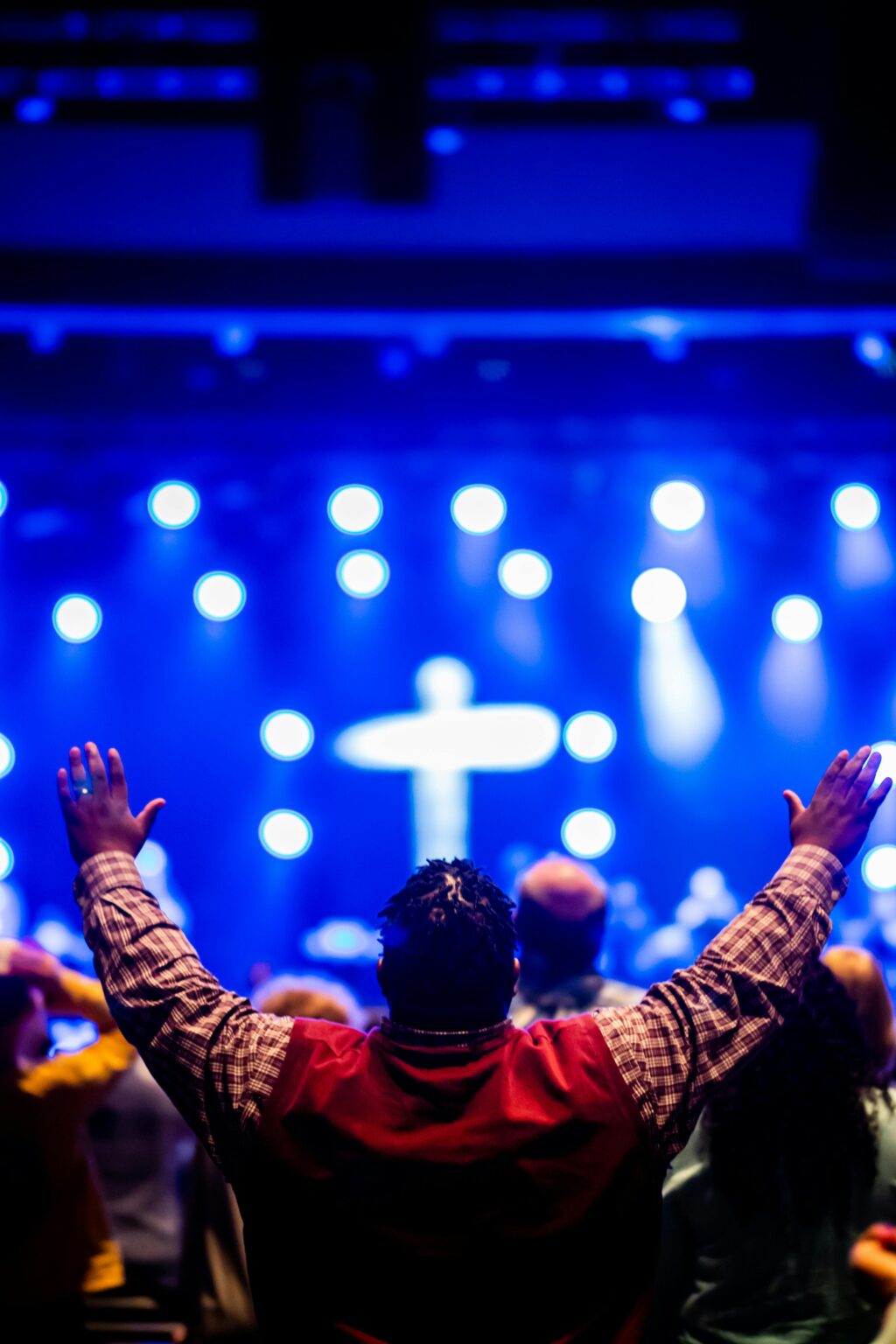 Crowd gathered in worship with a focus on a cross and dynamic stage lighting.